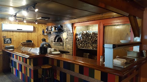 A wooden bartop with stacks of wood behind it and a brick pizza oven