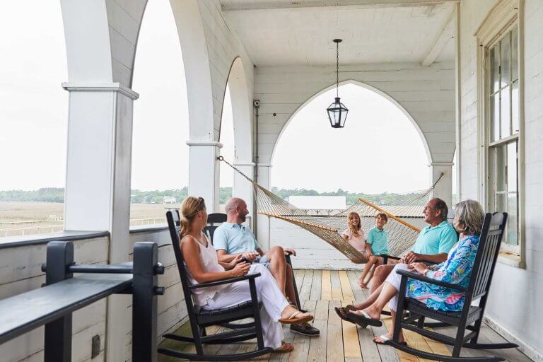 A family relaxes in rocking chairs and a hammock on a white arched porch