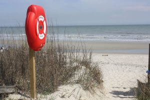 A red life ring station on a post at the entrance to a sandy beach on Pawleys Island, SC
