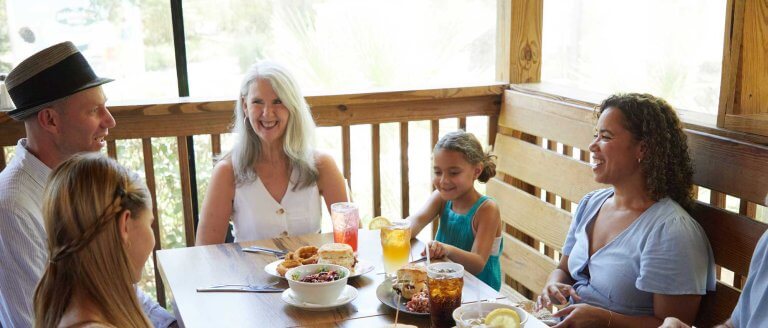 A family laughs and enjoys a meal together at an outdoor table at Pawleys Island, SC