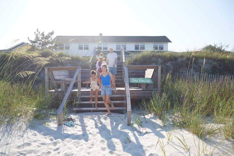 A family walks down wooden stairs from the Sea View Inn onto a sunny beach on Pawleys Island