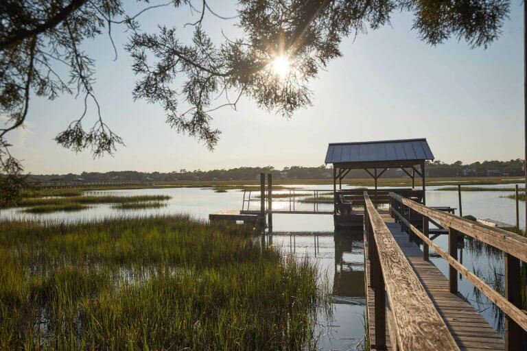 A wooden dock and pavilion overlook a sunlit marsh off Pawleys Island, SC at golden hour