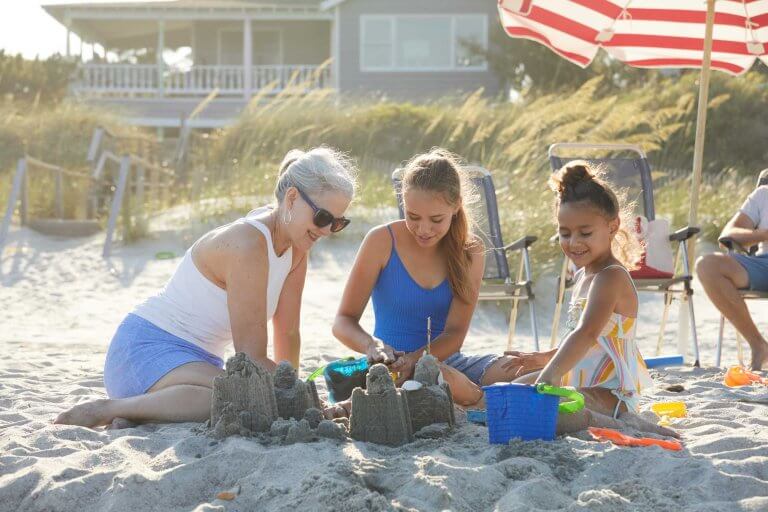 A woman and two girls build a sandcastle together on a sunny Pawleys Island, SC beach