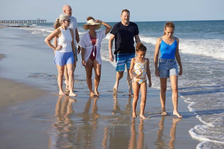 A family walks together along the Pawleys Island shoreline with a pier in the distance