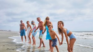 A multi-generational family holds hands and smiles while wading in the ocean surf at Pawleys Island